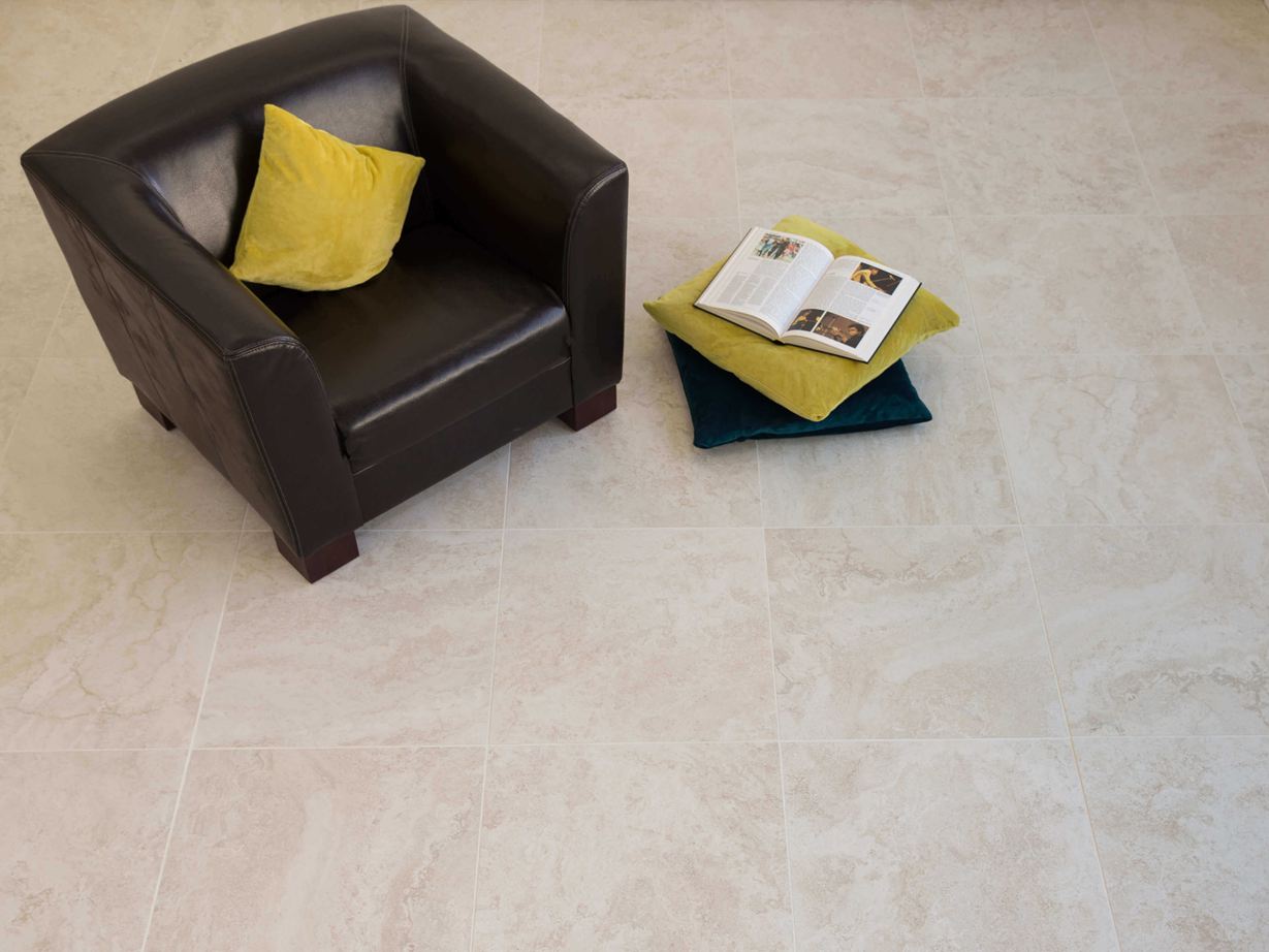 Carreaux en grès cérame fin, aspect travertin clair avec fauteuil noir et coussins colorés.