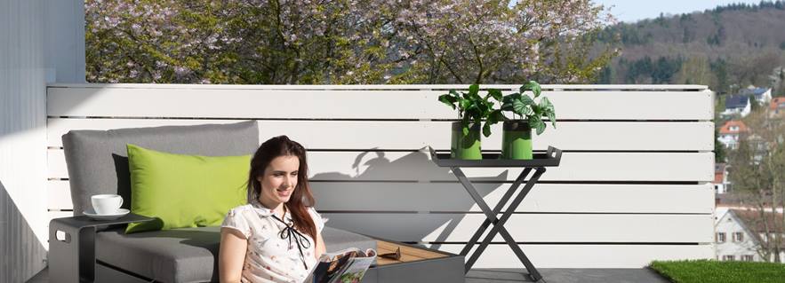 Femme assise sur la terrasse avec des dalles grises d'aspect ardoise et un mobilier moderne.