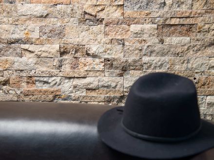 Un chapeau noir posé sur un canapé devant un mur en plaquettes de parement en travertin Scabas
