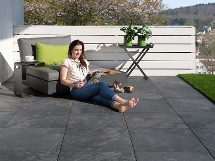Une jeune femme lit sur une terrasse en dalles imitation ardoise Alpine Black
