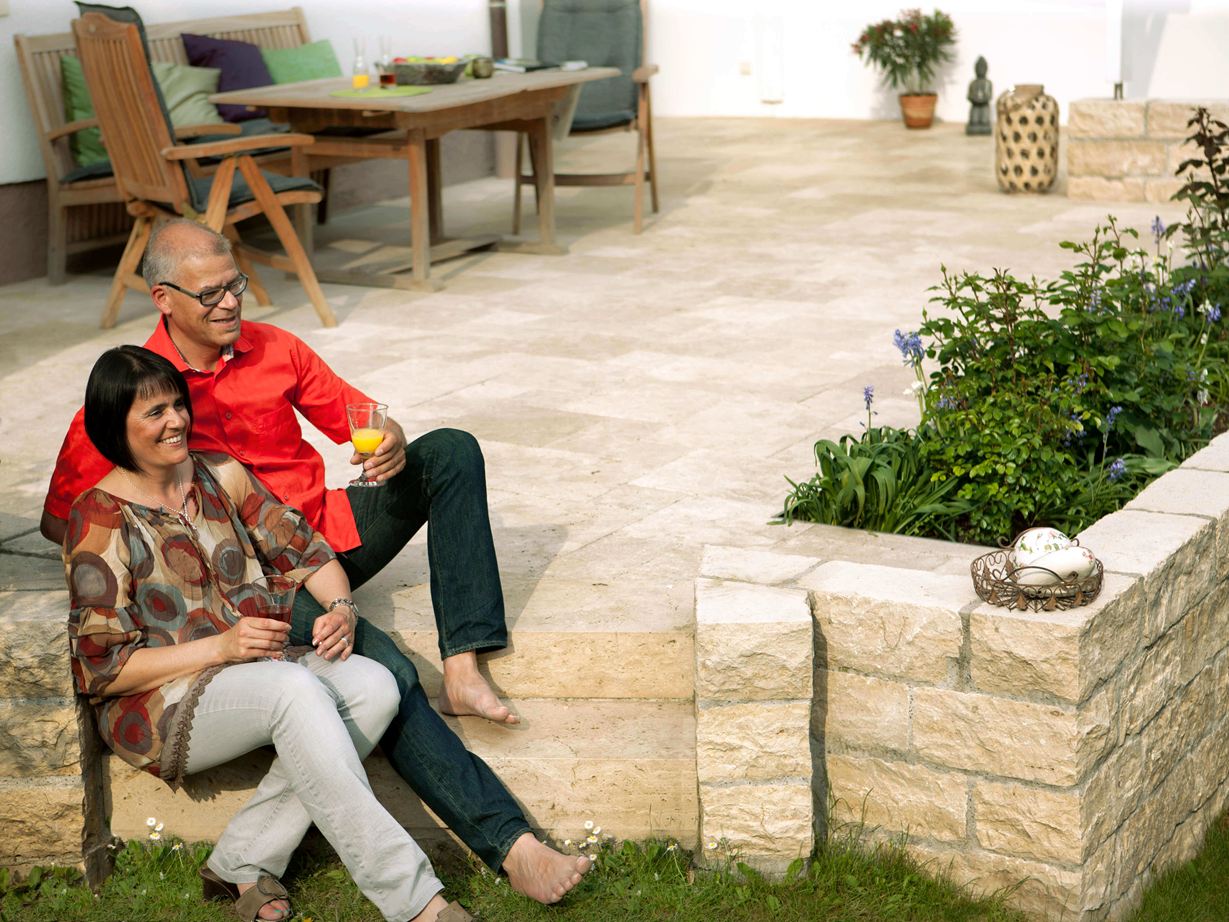Un plaisir au toucher, tout particulièrement pieds nus Couple assis sur terrasse en travertin Medium SELECT, mur en pierre naturelle, mobilier de jardin en bois
