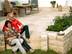 Couple assis sur terrasse en travertin Medium SELECT, mur en pierre naturelle, mobilier de jardin en bois