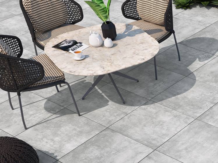 Le revêtement de sol en grès cérame de couleur claire, aspect béton, sur une terrasse décorée d'une table et de chaises de jardin