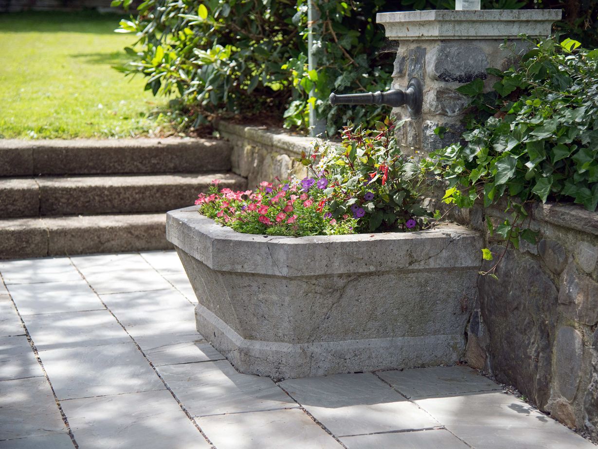 Cette fontaine fleurie met la teinte grise des dalles en valeur Dalle de grès gris Kandla Grey avec fontaine fleurie