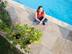 Une femme assise en tailleur sur le dallage en grès au bord de la piscine, photographiée d'en haut