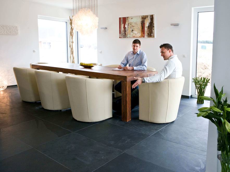 Table de salle à manger avec fauteuils blancs et deux personnes sur carrelage d'ardoise Mustang en gris foncé