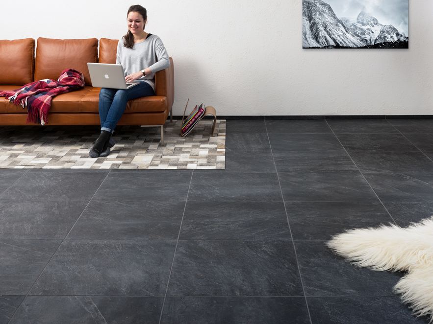 Salon avec carrelage en effet ardoise, une femme assise avec ordinateur portable sur un canapé marron.