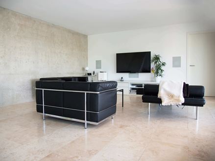 Salle de séjour moderne avec canapé noir et carreaux de travertin beige clair Classic Light comme revêtement de sol