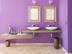 Salle de bain avec mur violet et deux miroirs, sol en carrelage en travertin Light à la finition vieillie