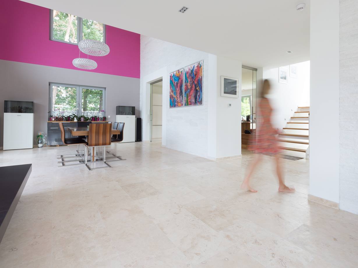 Sa couleur est parfaite pour tout style d'intérieur. Salle à manger lumineuse avec des meubles modernes, des carreaux de travertin Classic Light lumineux comme revêtement de sol et un mur rose à l'arrière-plan.