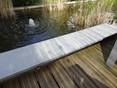 Un étang semi-ombragé, avec des planches de bois et des dalles de granit à l'avant comme bord de l'étang.