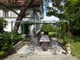 La terrasse en grès Kandla Grey est accueillante. Terrasse Kandla Grey en grès avec un salon de jardin en bois, une fontaine fleurie et de la verdure tout autour