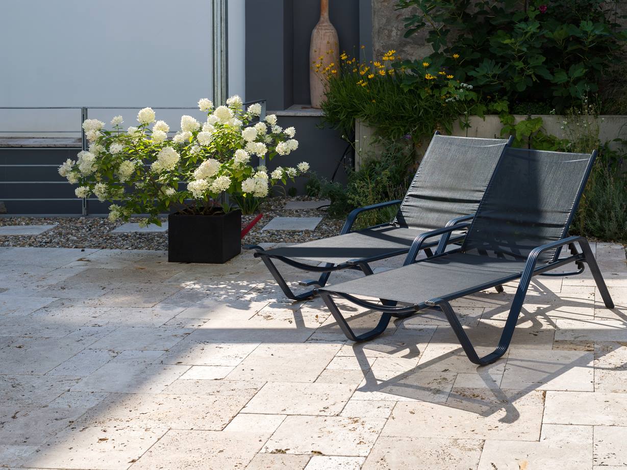 La dalle Rustic a une aura très relaxante. Terrasse en travertin Rustic avec deux chaises longues et un pot de fleurs