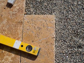 Dalles de travertin dans un lit de gravillons fins, à côté duquel se trouve un niveau à bulle.