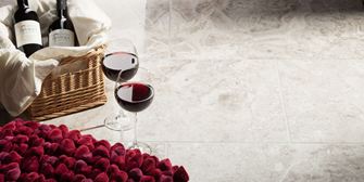 Zwei Weingläser stehen neben gefülltem Erdbeerkorb auf Marmorfliesen Silver Shadow poliert