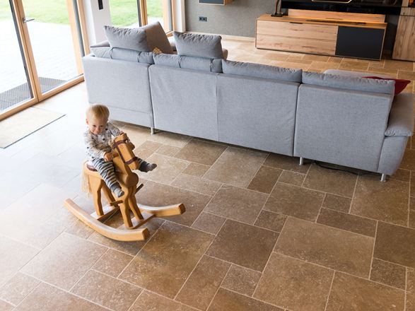 Kind sitzt auf Schaukelpferd und spielt im Wohnzimmer mit Travertinboden Noce SELECT