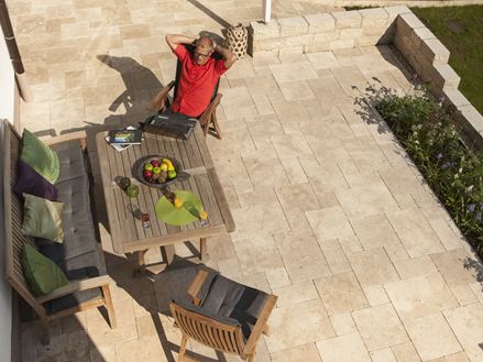 Homme assis à la table du jardin sur une terrasse avec du travertin léger en opus romain